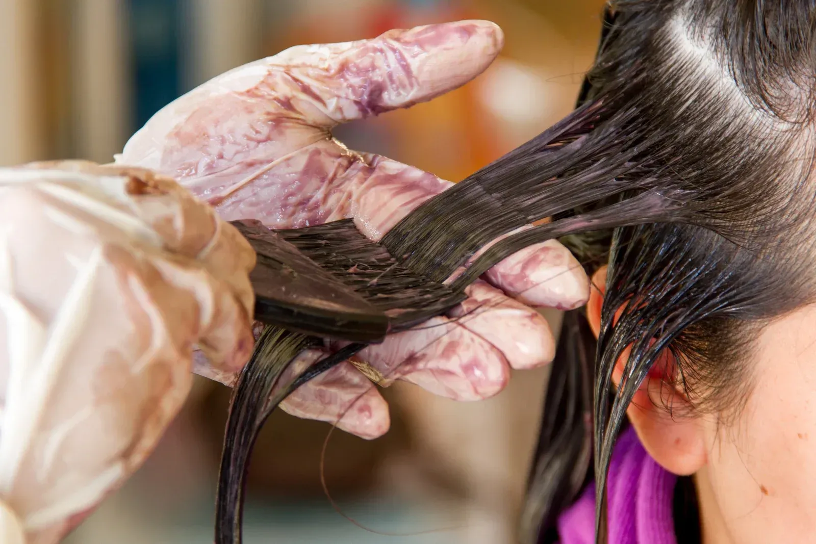Person applying hair dye with gloved hands. Dark hair, purple highlights.