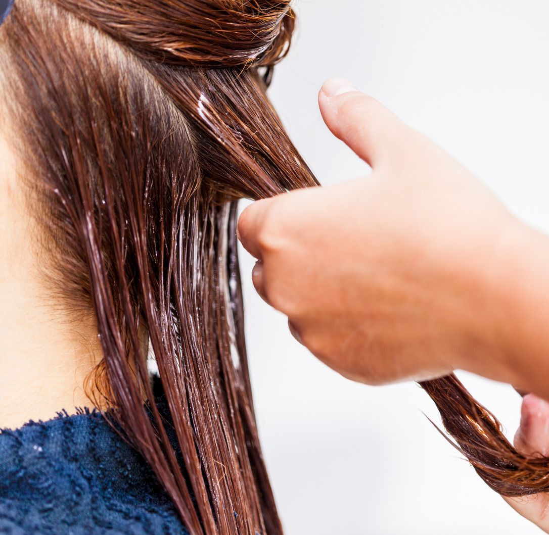 Person applying hair product to wet, brown hair with hands.