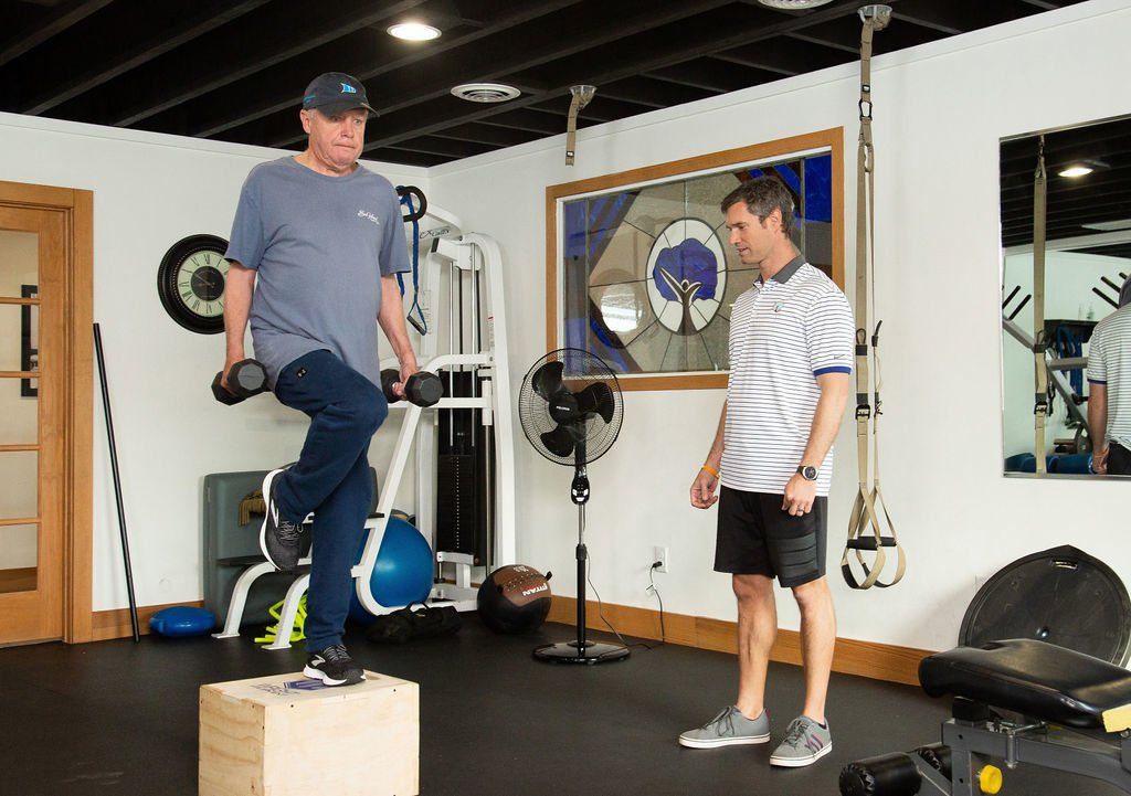 A man is standing on a box in a gym while another man looks on.
