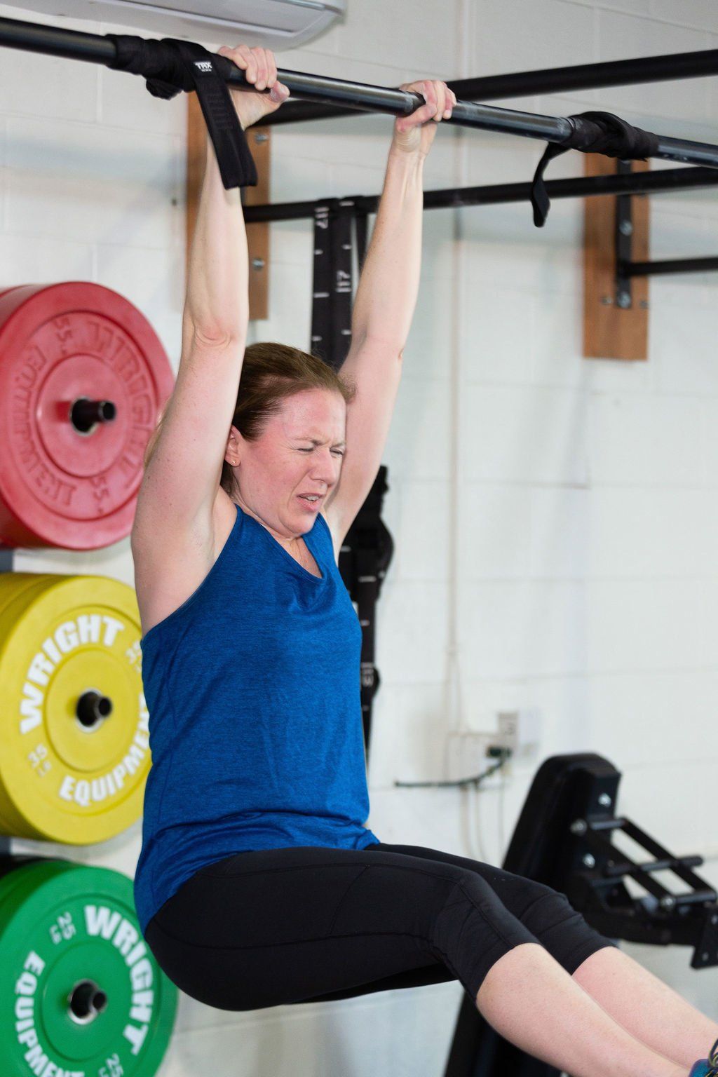 A woman is doing a pull up on a bar in a gym