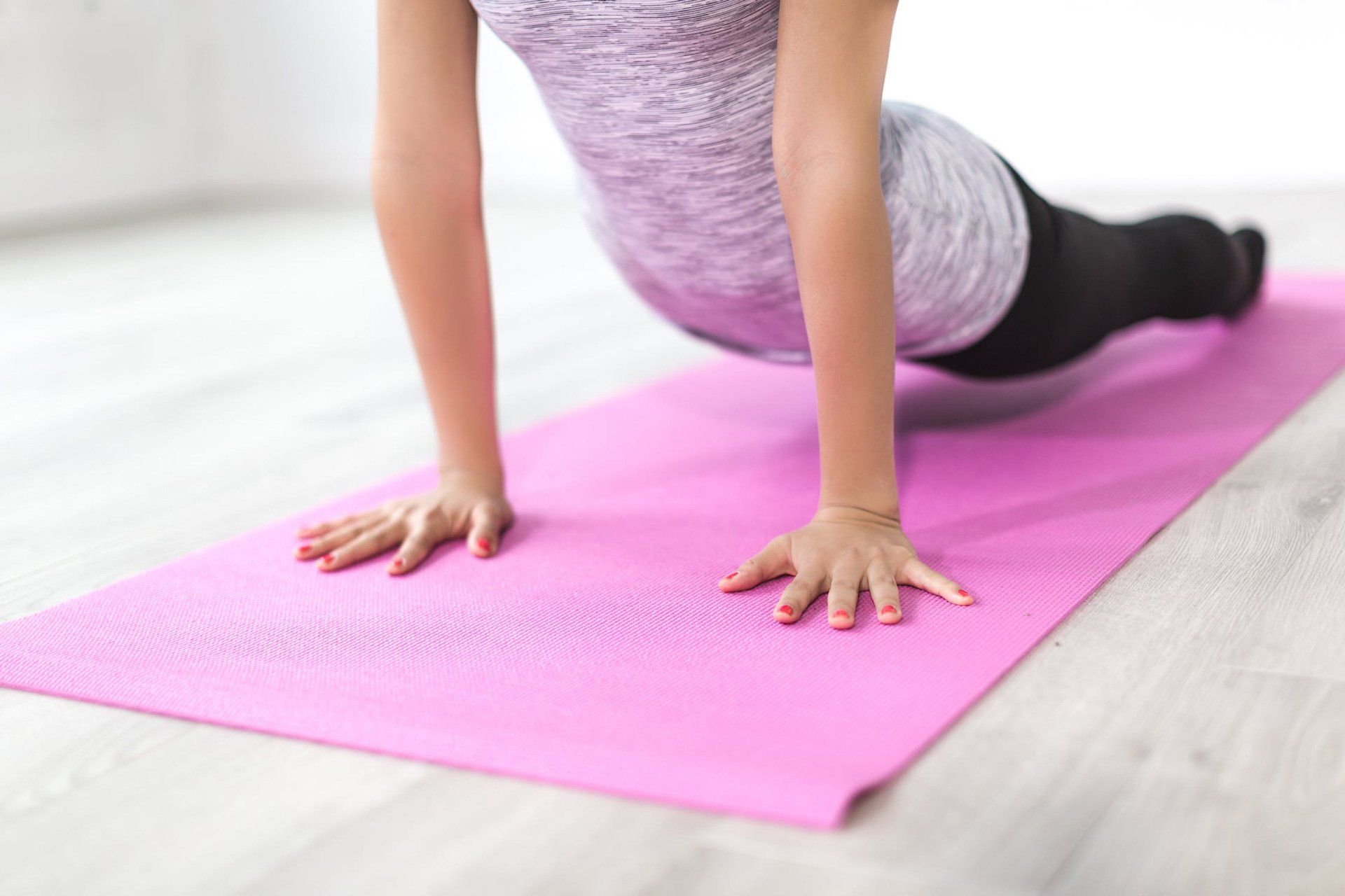 A woman is doing push ups on a pink yoga mat.