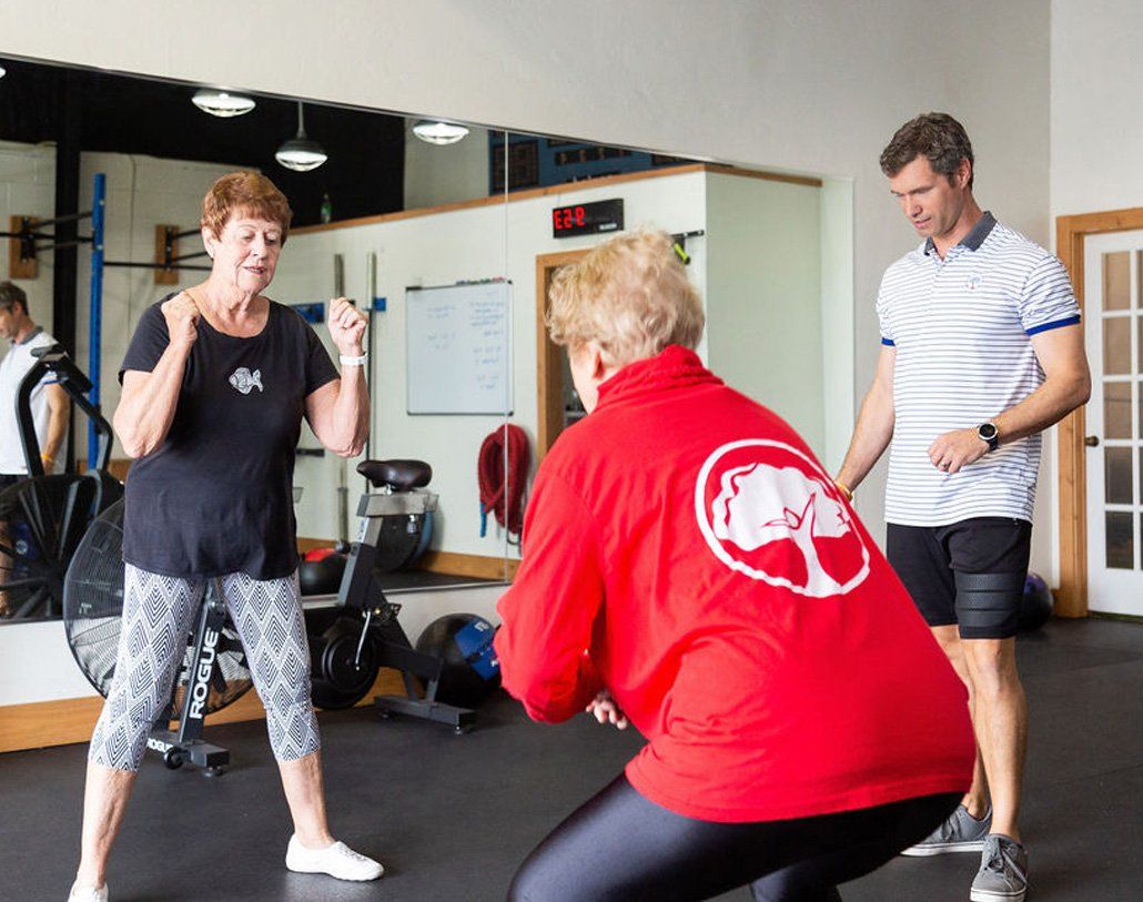 A woman in a red shirt is squatting in a gym