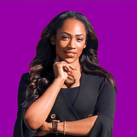 A woman is standing with her arms crossed in front of a purple background.