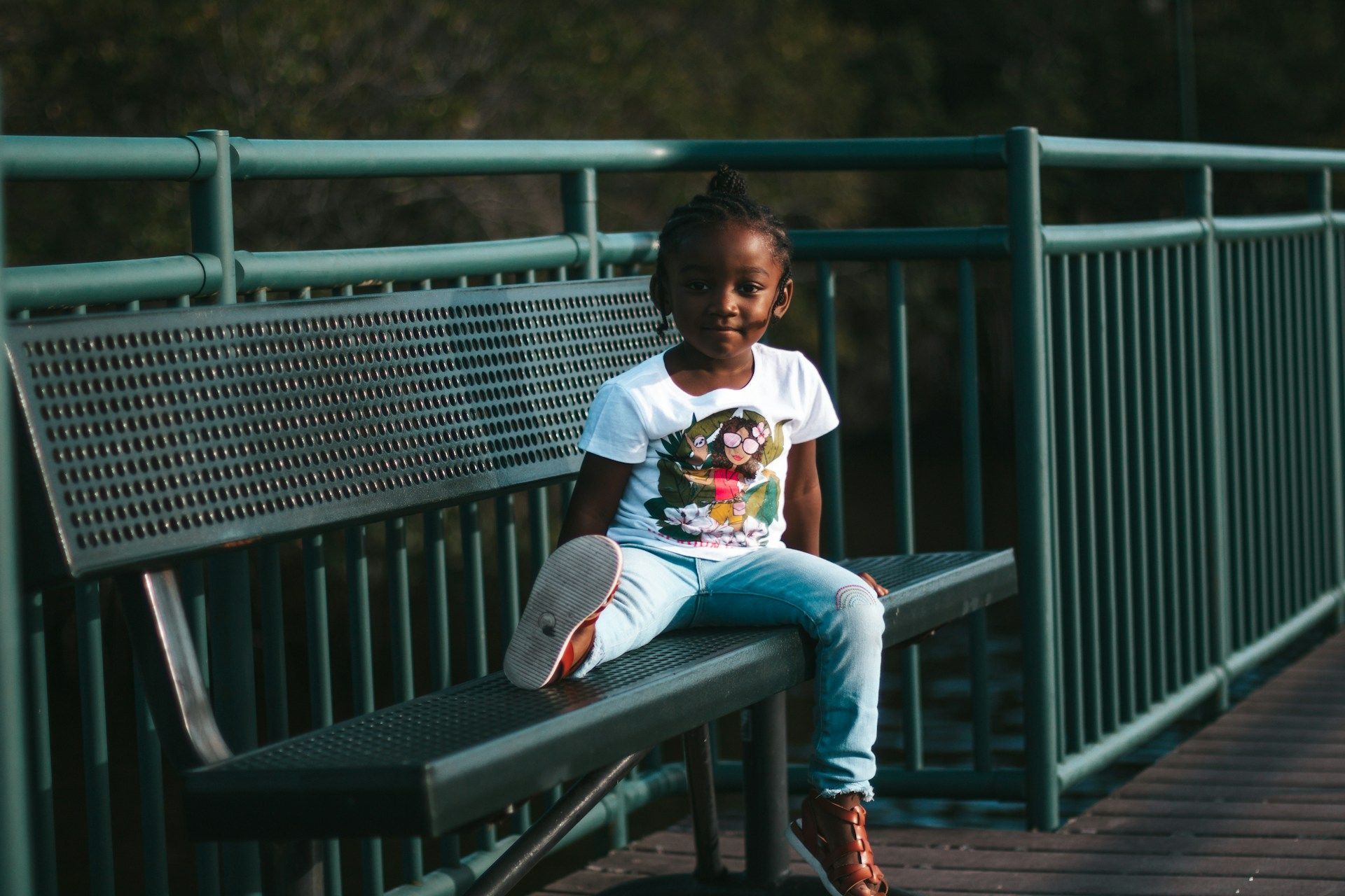 A little girl is sitting on a bench on a bridge.