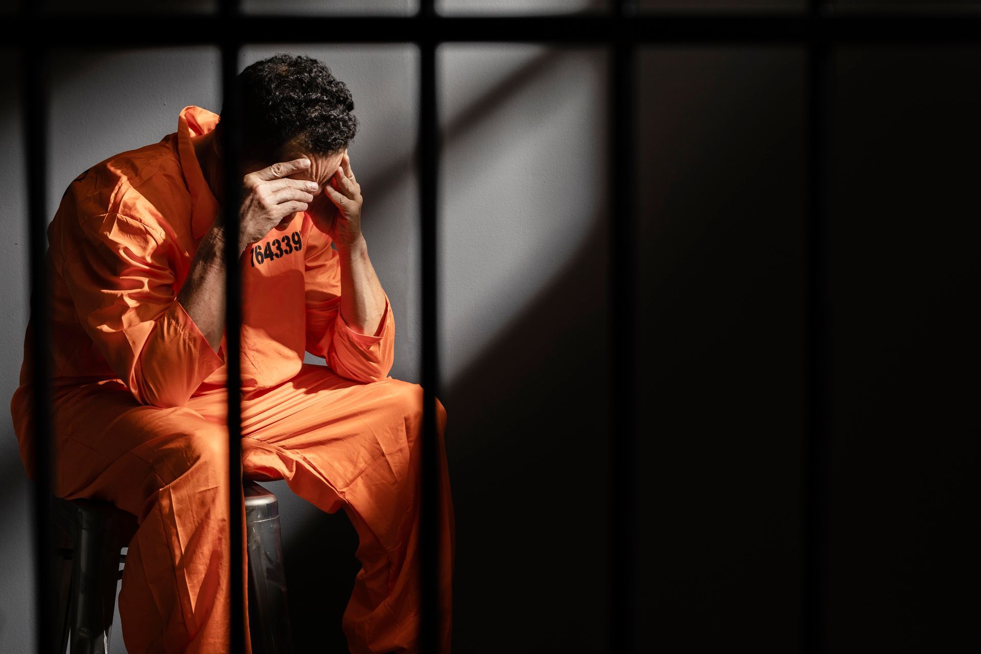 A man in an orange jumpsuit is sitting in a prison cell.