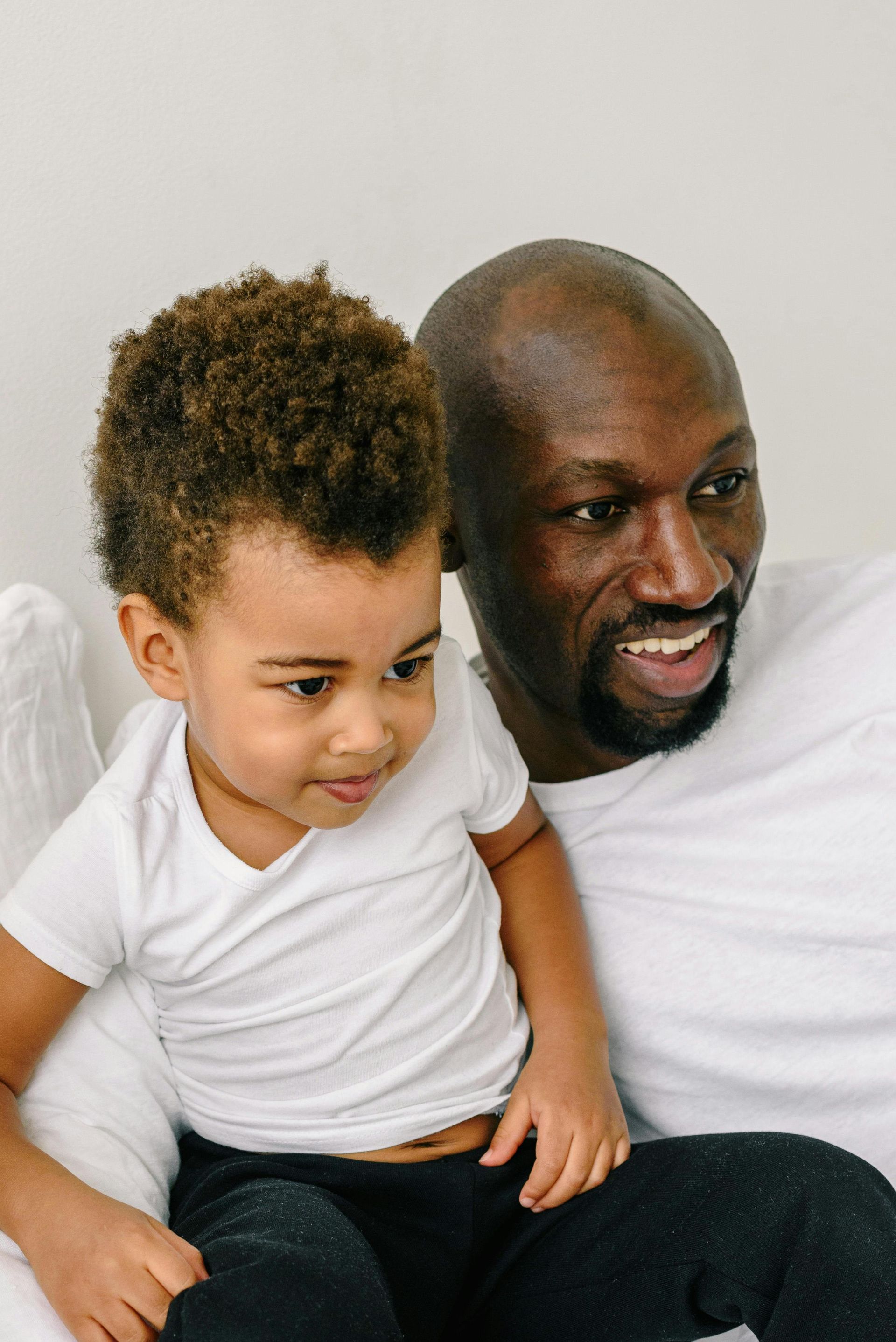 A man and a little boy are sitting next to each other on a bed.