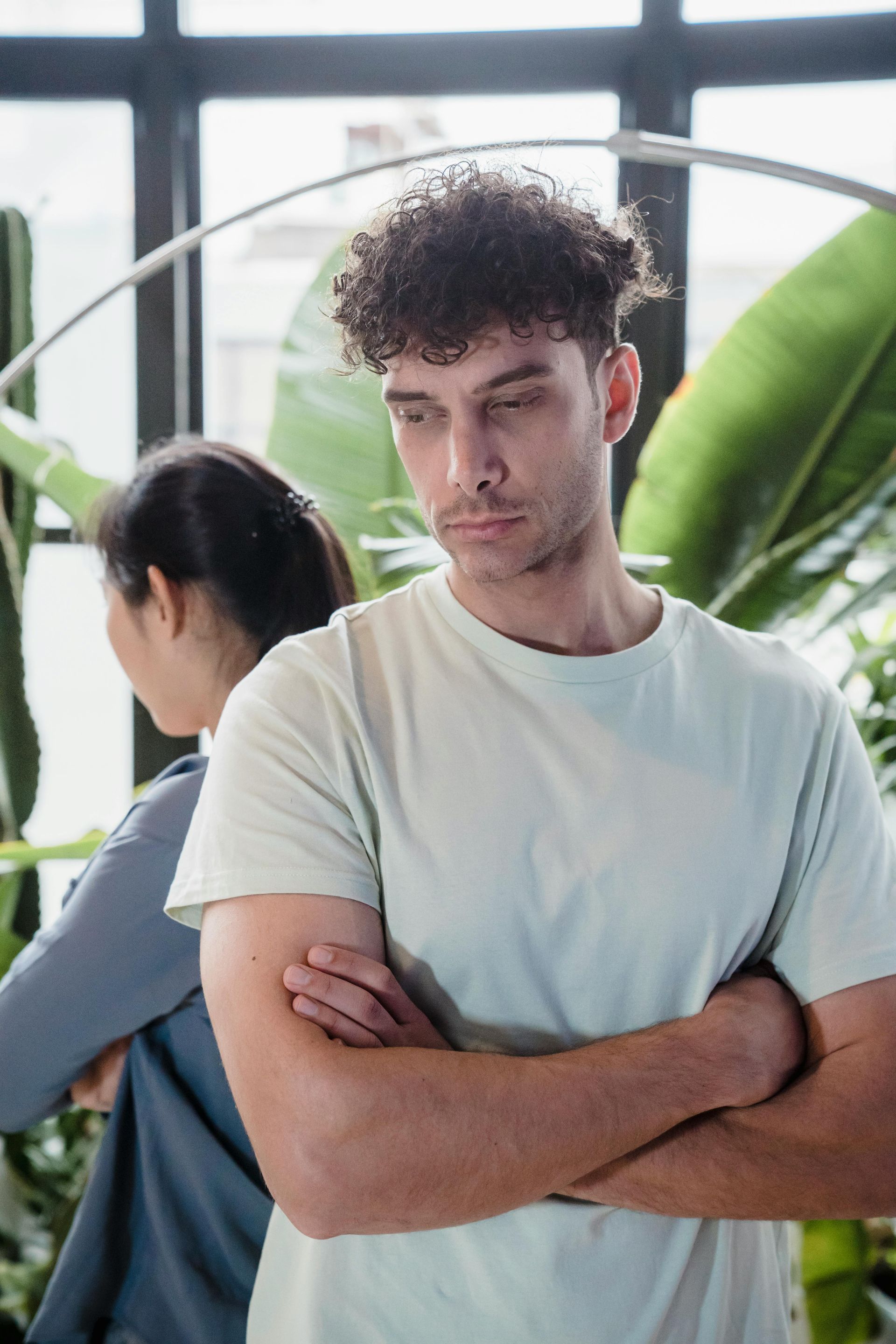 A man and a woman are standing back to back with their arms crossed.