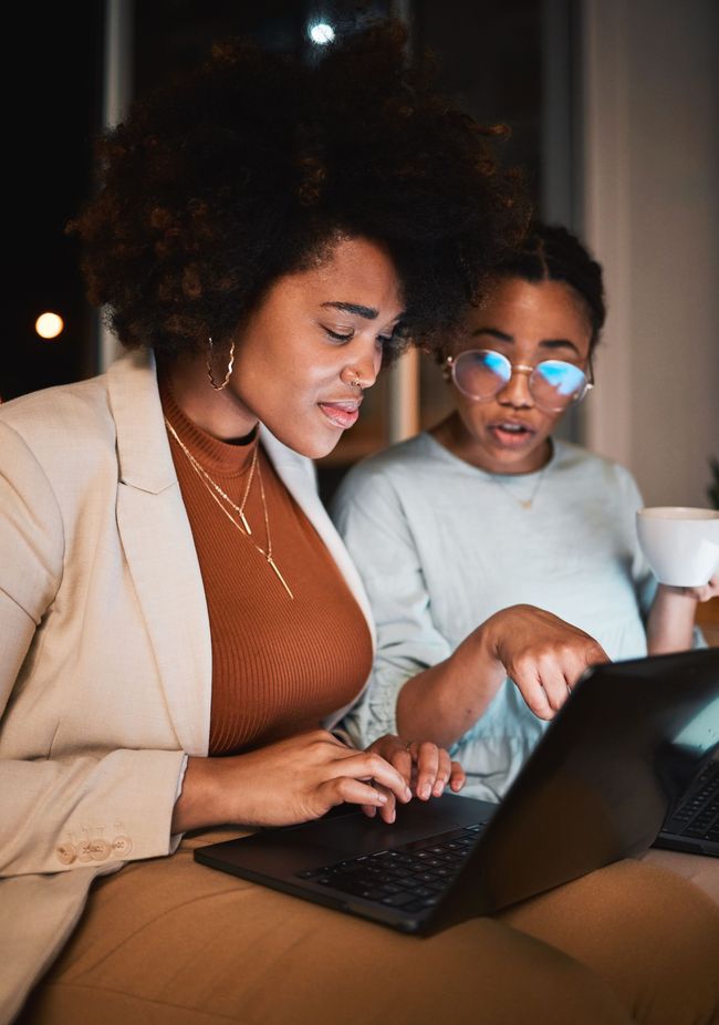 Two women are sitting at a table looking at a laptop computer.