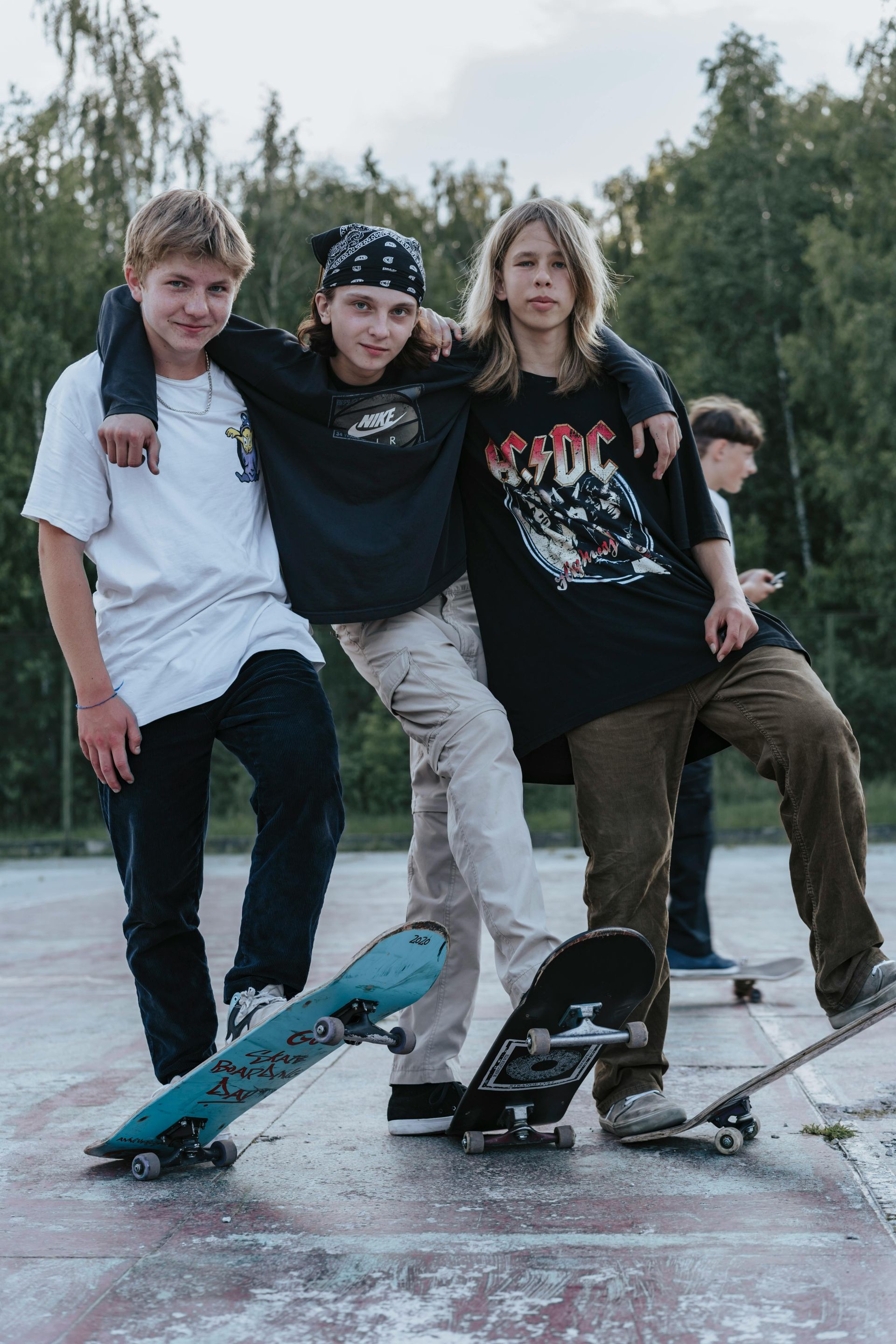 Three young people stand together on an outdoor court, each with their feet resting on their skateboards.