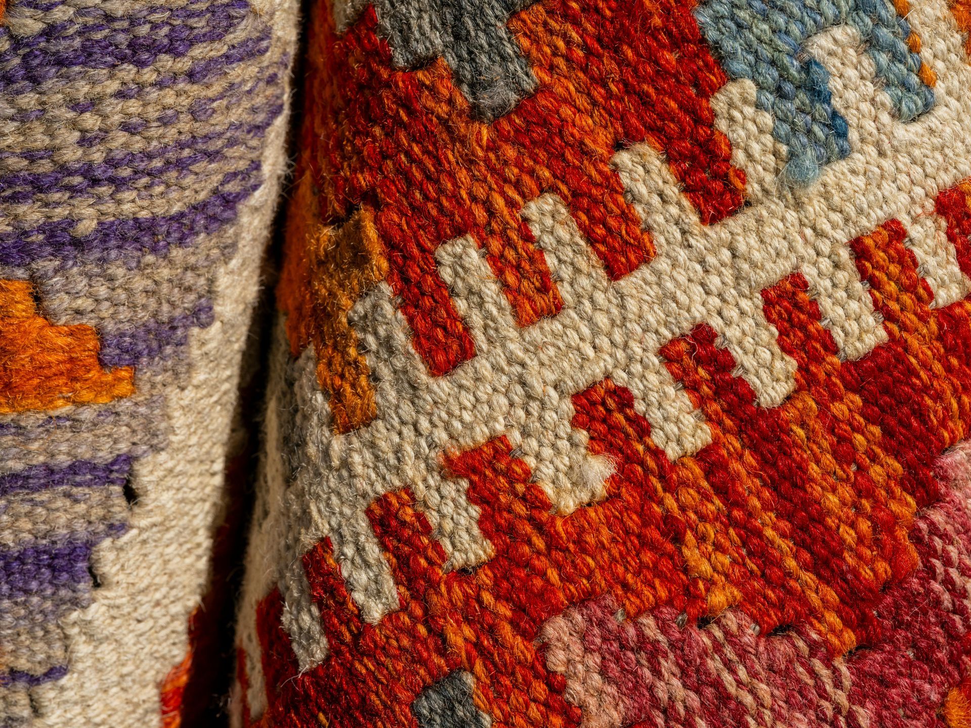 An assortment of overlapping traditional, ornate rugs in shades of red, blue, and gold with intricate geometric patterns.