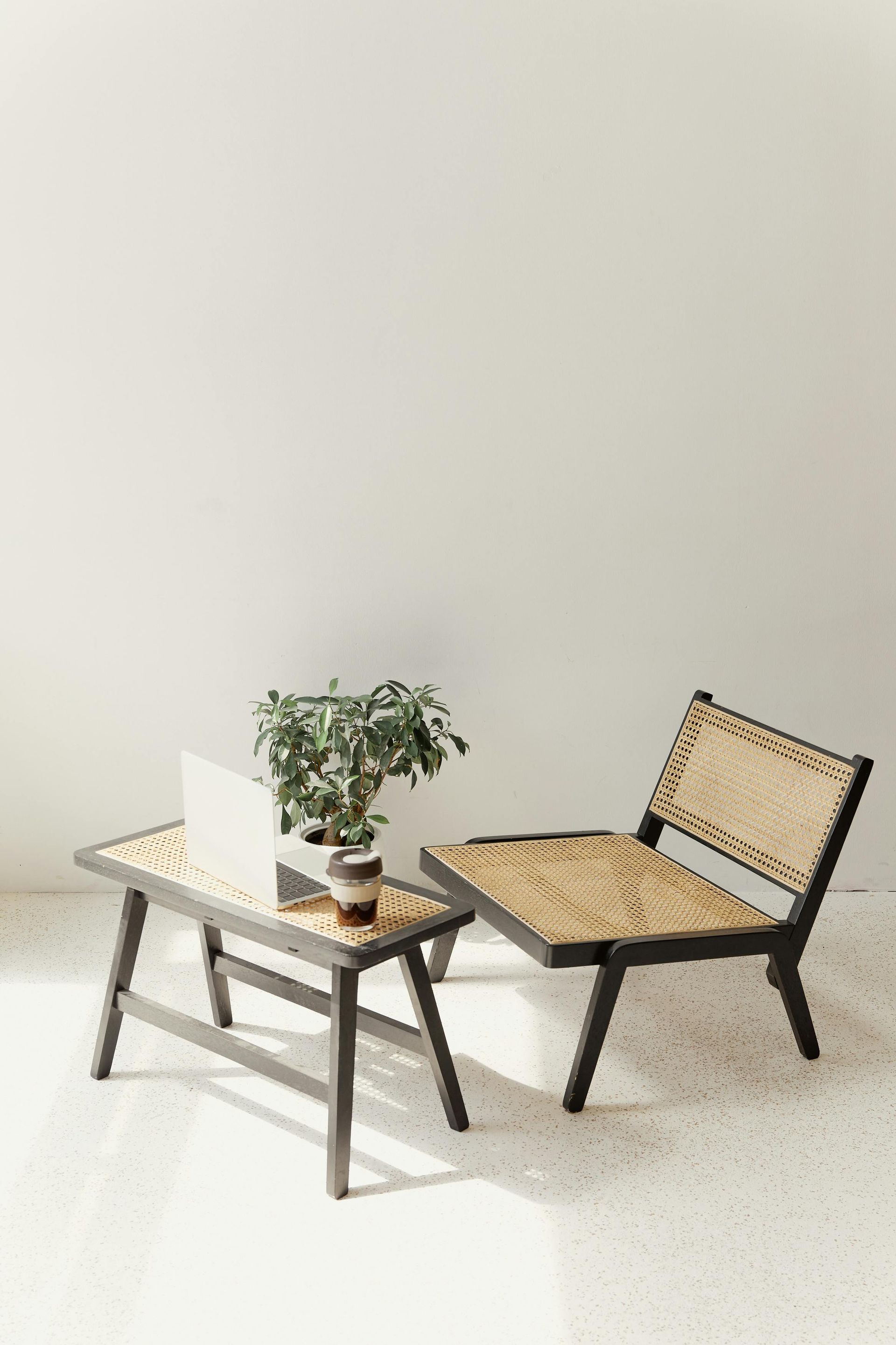 Chair and table with woven seats; laptop and plant on table, against a white wall.