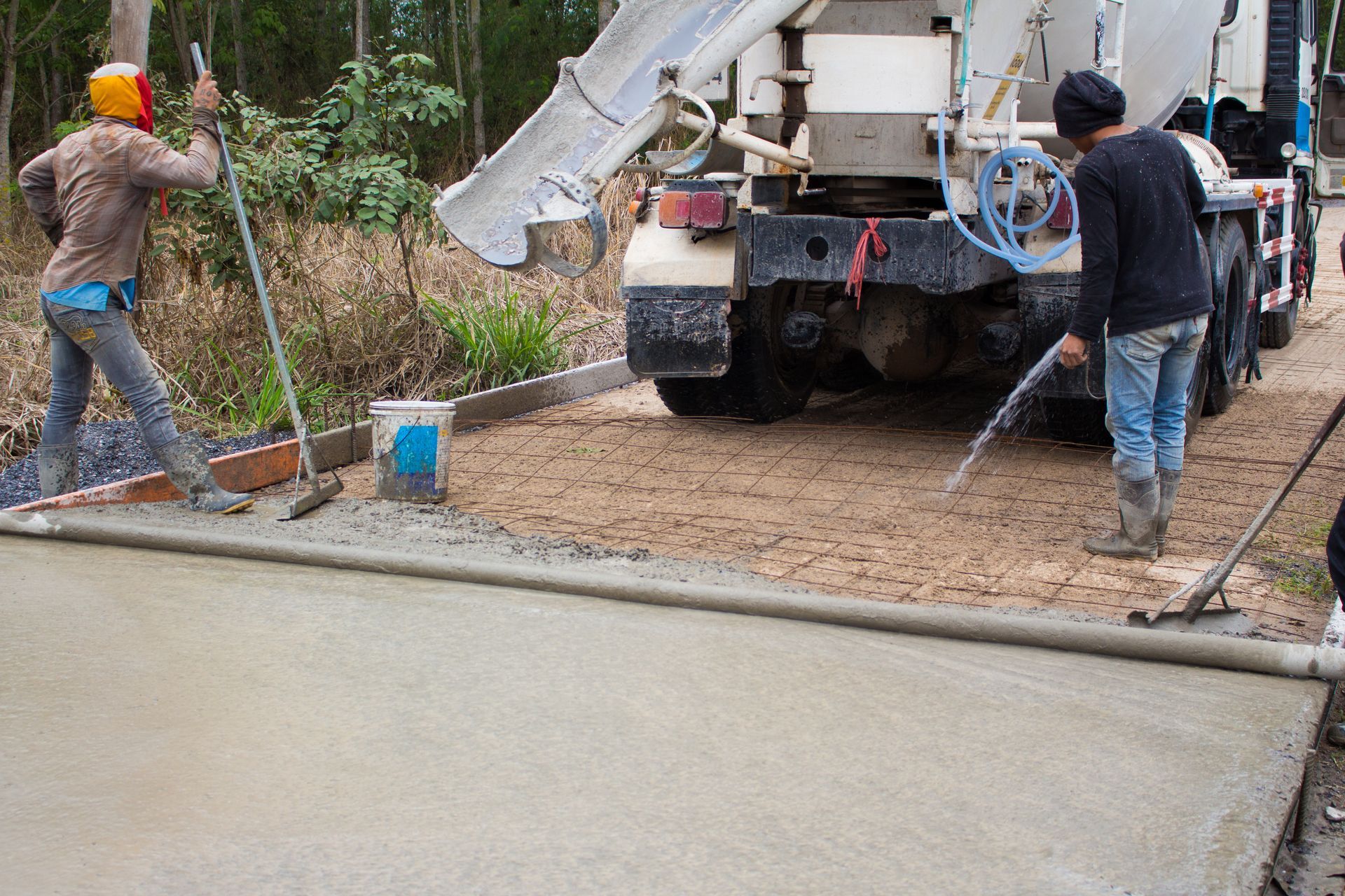 Workers pouring concrete from a truck onto a prepared surface, spreading and smoothing it.