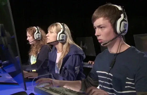 Paintbrush mixing dark brown paint on a wooden artist's palette with various colorful paint splotches.