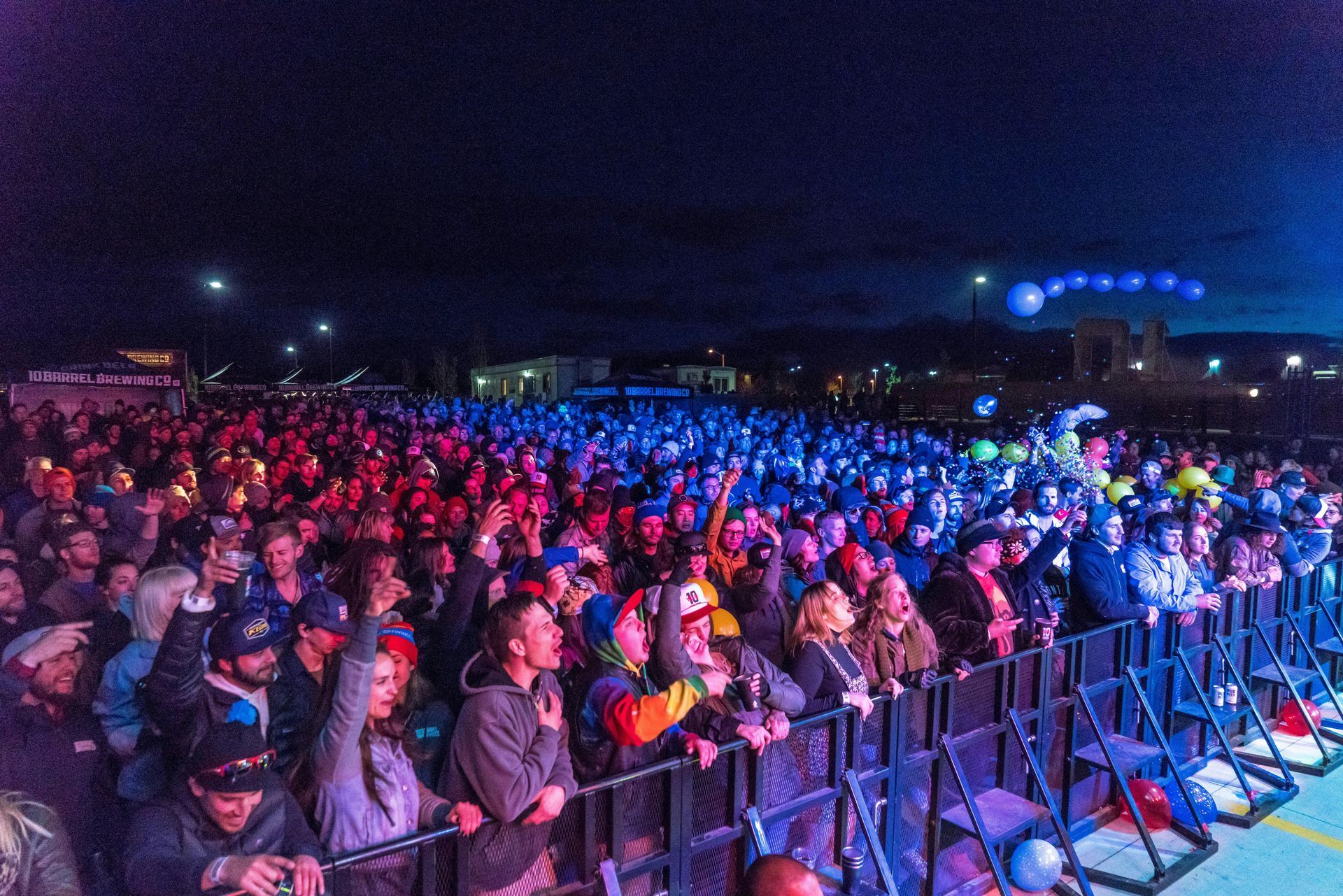 Crowd at a nighttime outdoor concert, lit with red and blue lights. People are watching a stage.