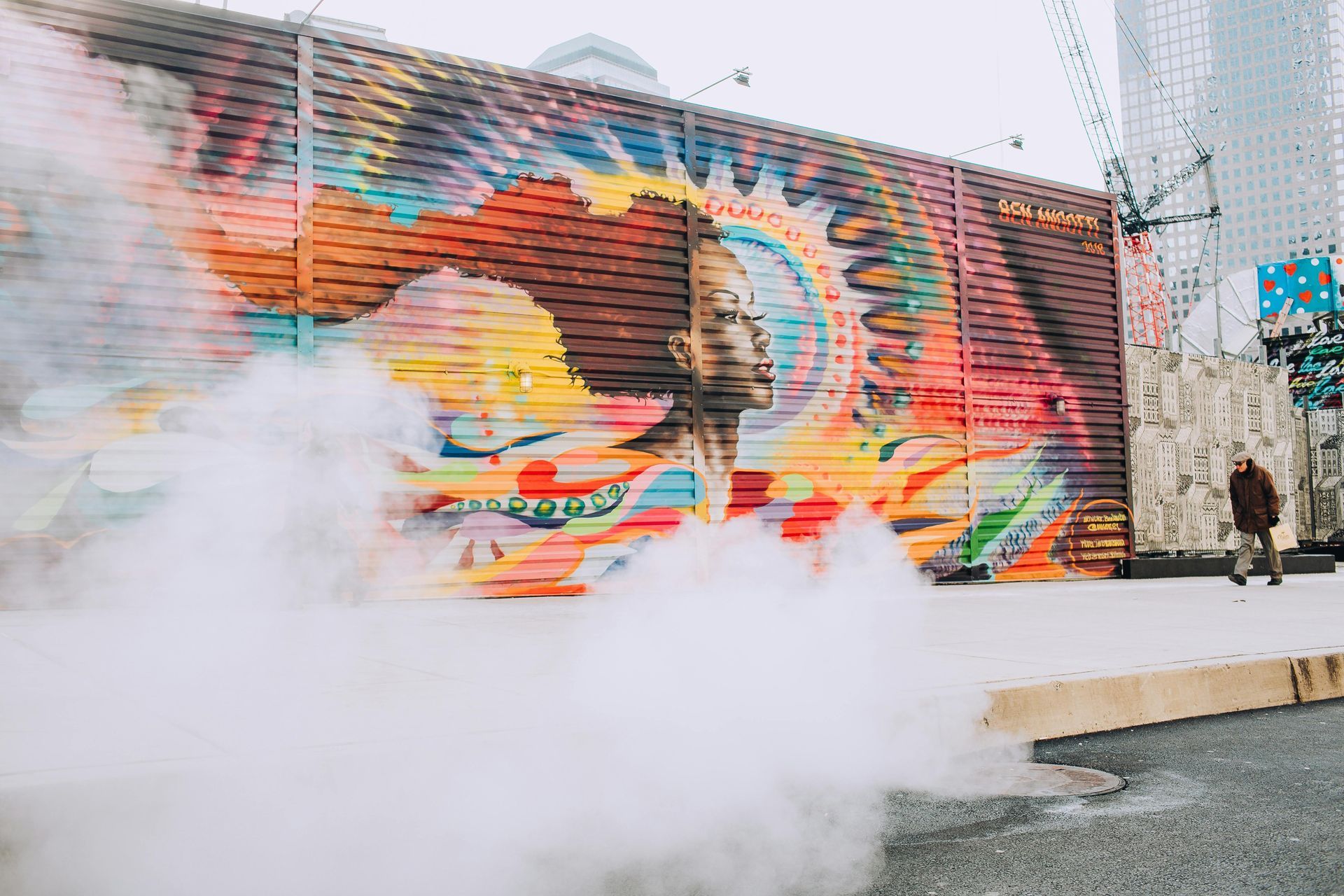Colorful mural with a person walking by steam rising from the street.