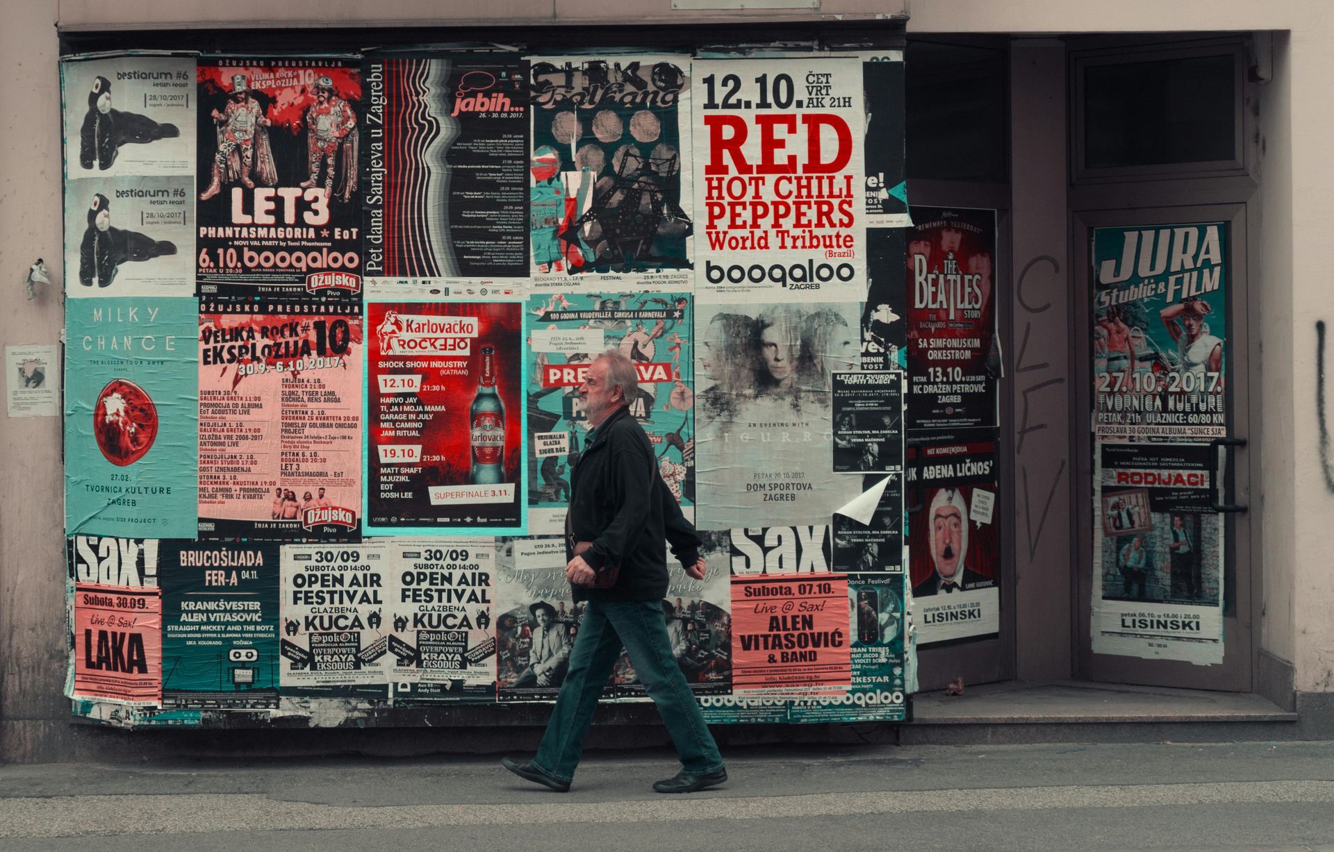 Man walks past a wall covered in colorful posters, including one for Red Hot Chili Peppers.