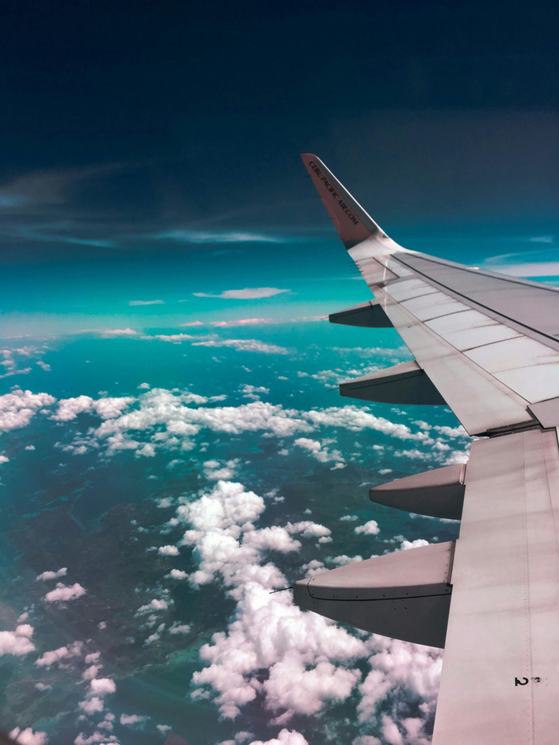 Airplane wing soaring above clouds and turquoise ocean.