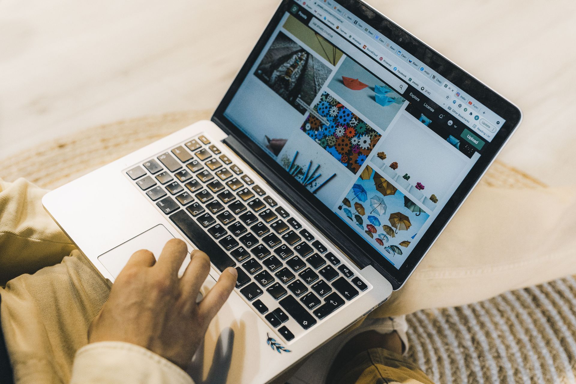 Person typing on a laptop showing a photo and design collage on a wooden table