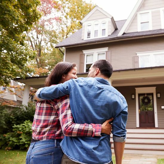 A man and a woman are hugging in front of a house.