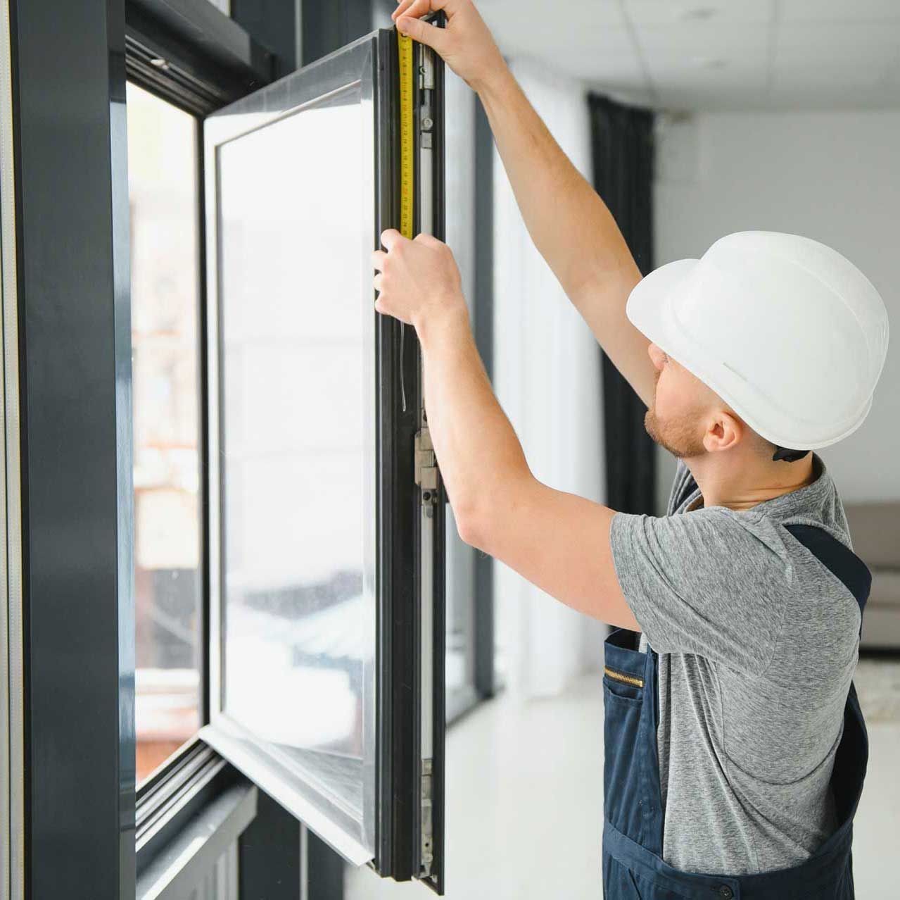 A man is measuring a window with a tape measure.