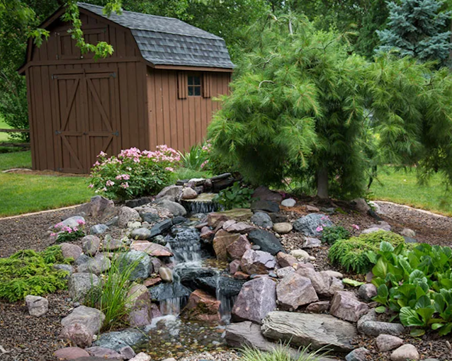A shed with a waterfall in front of it in a garden.