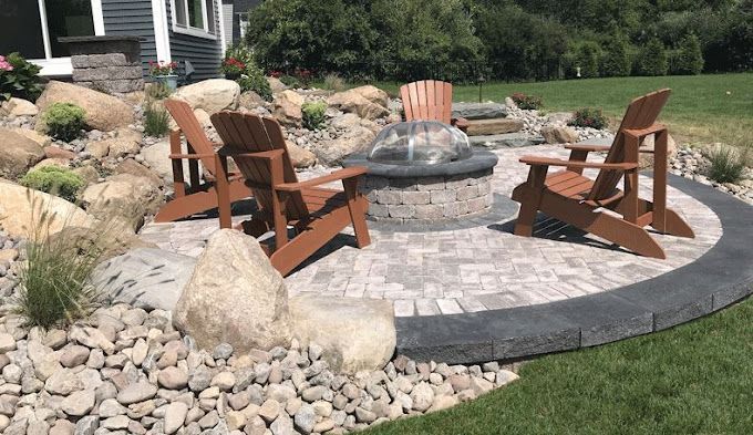 A fire pit surrounded by rocks and chairs in a backyard.