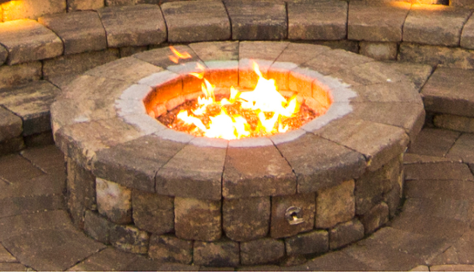 A fire pit is surrounded by bricks and has a fire coming out of it.