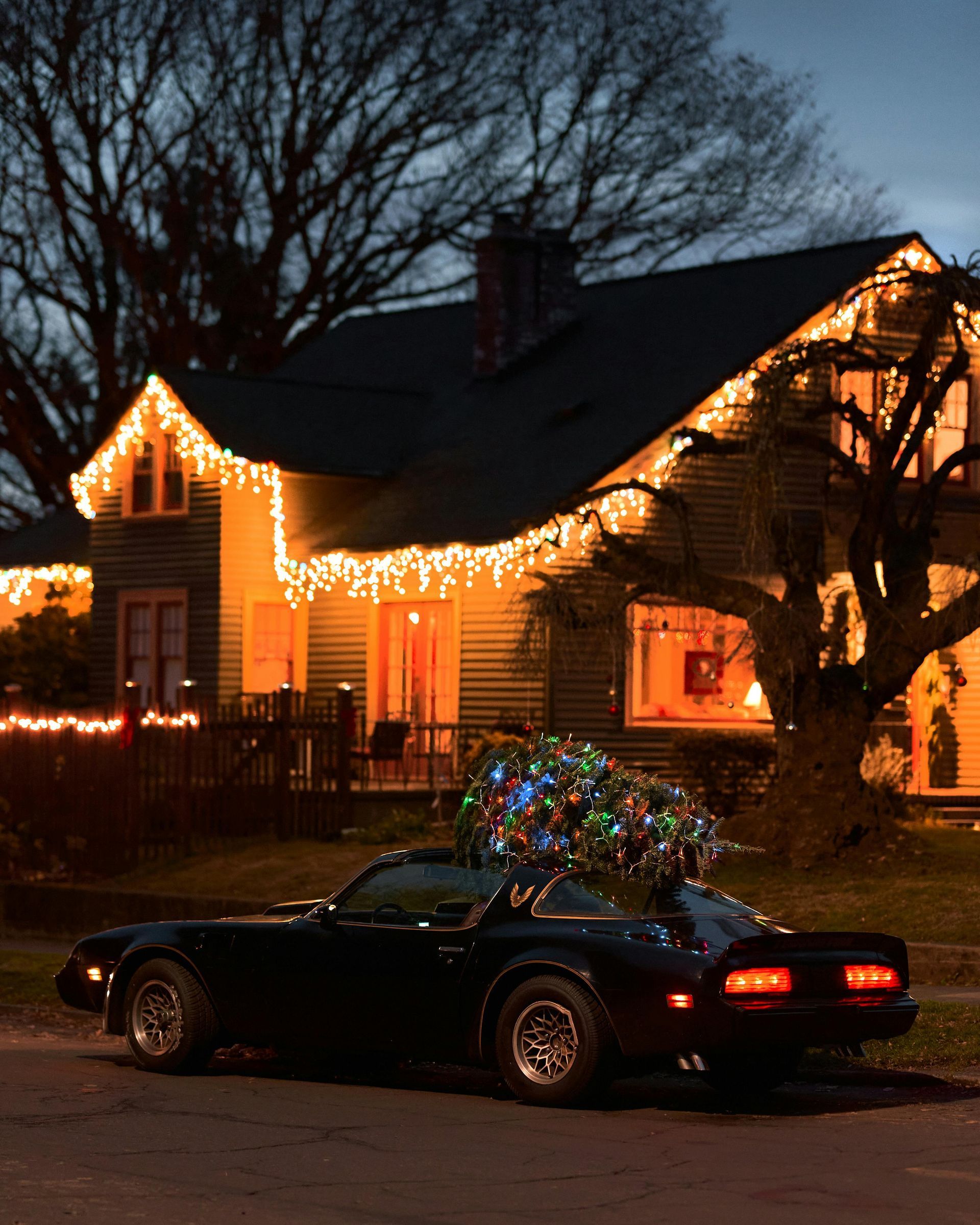 A black car is parked in front of a house decorated for christmas