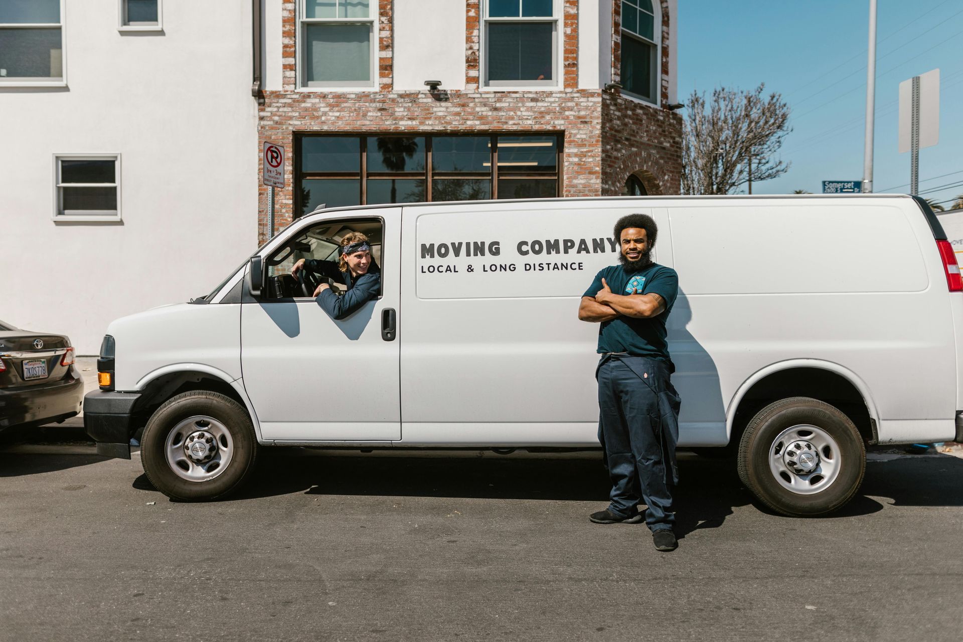 Delivery van with man standing beside it and a person sitting in driver seat looking out of the window