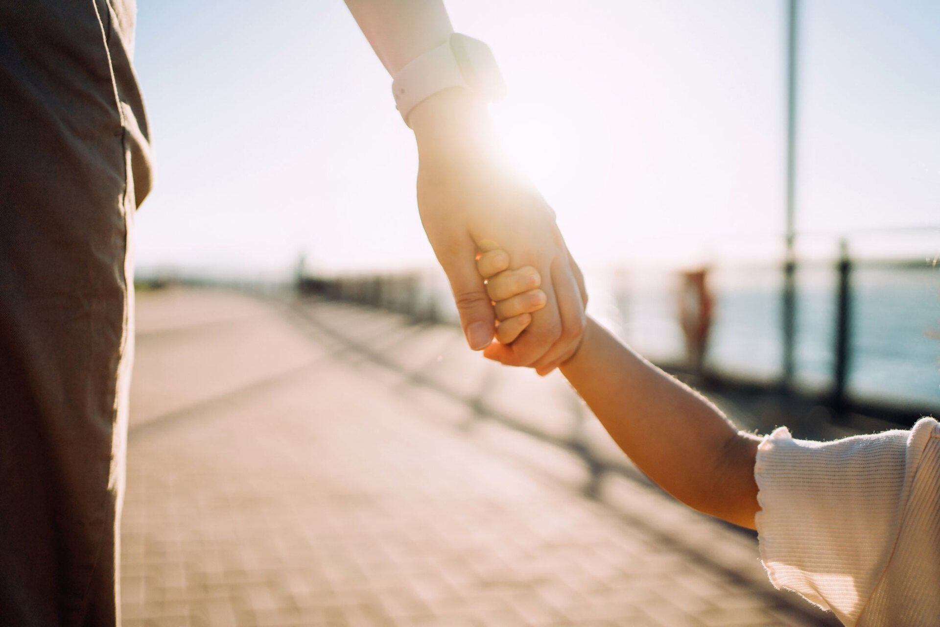 Parent holding child's hand on sunny day — Jacksonville, FL — Beaches Family Law