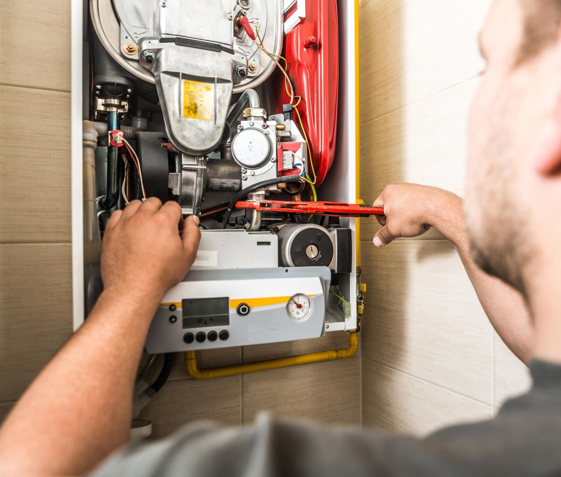 Person repairing a furnace with a wrench; indoor setting.