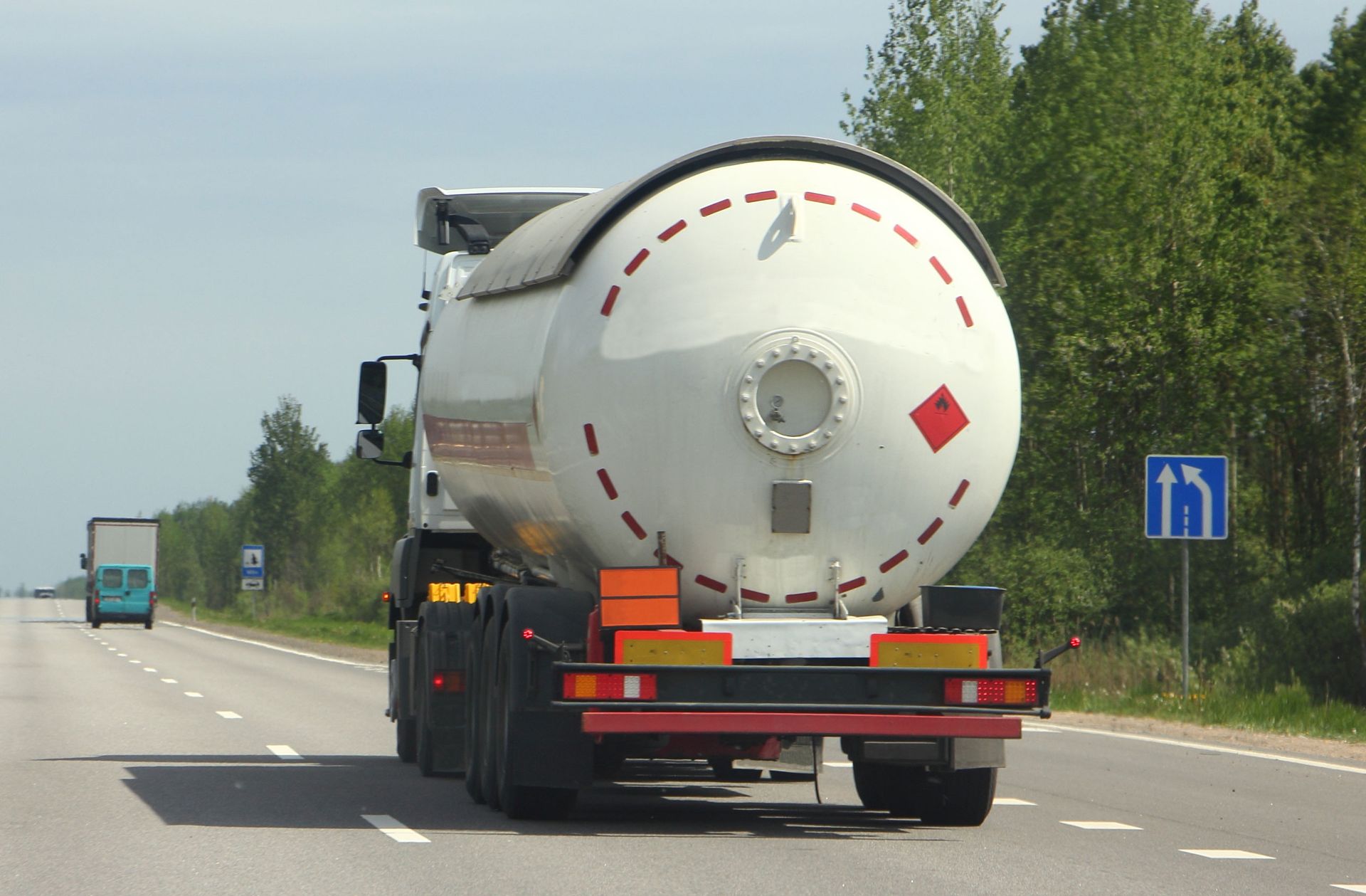 Tanker truck on a highway, transporting a cylindrical white tank with red hazard diamonds.