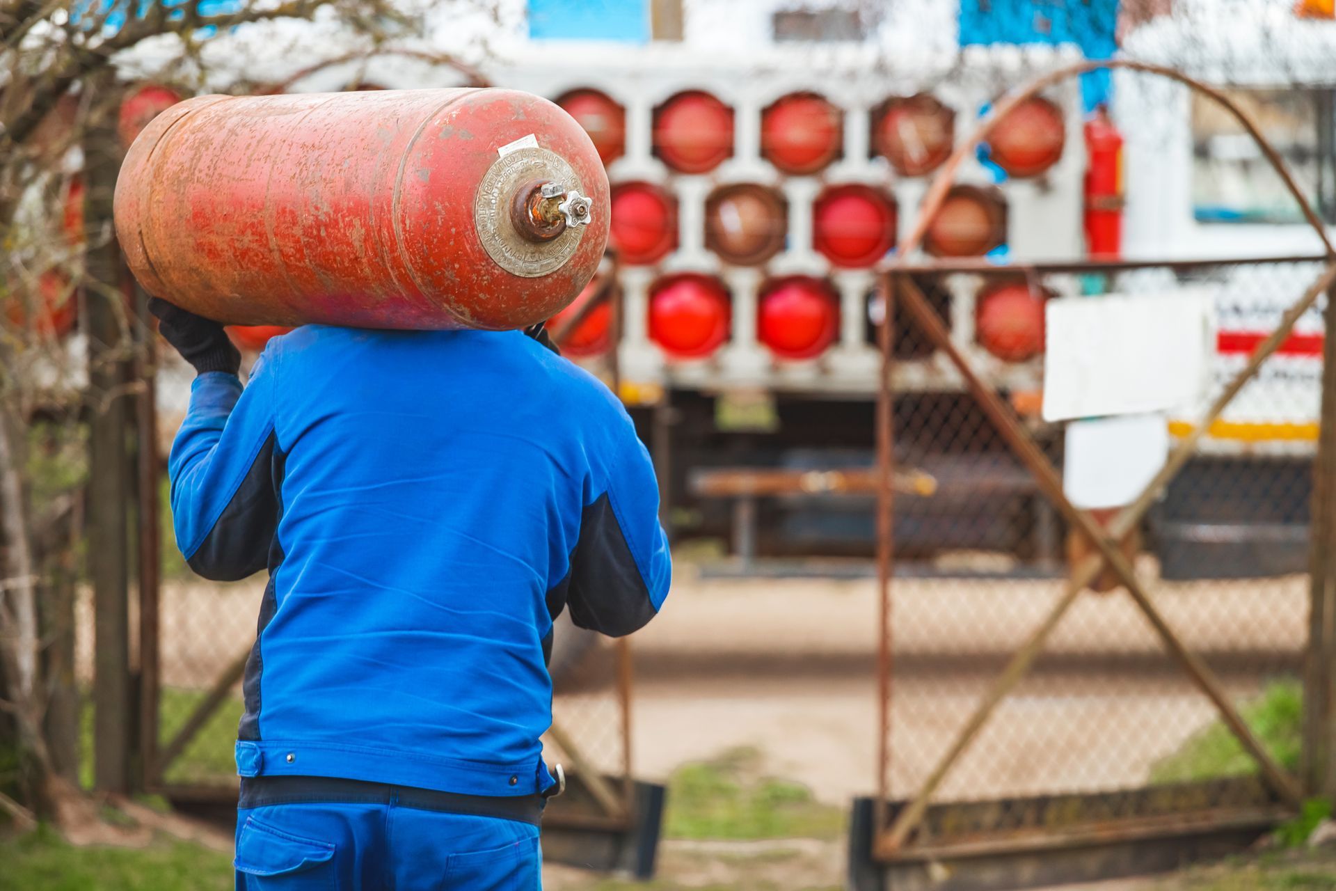 Worker carrying propane tank for residential delivery service.
