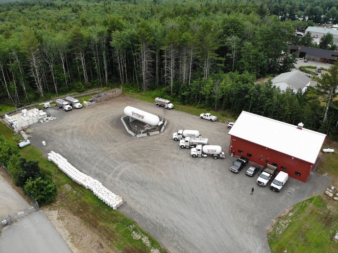Tanker truck on a highway, carrying a large silver tank, red cab, and taillights illuminated.