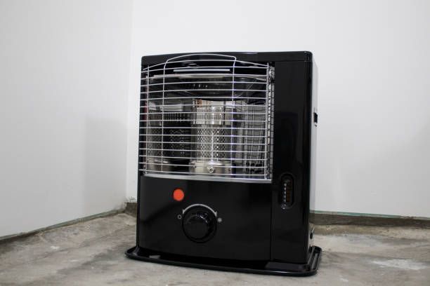 Black kerosene heater on a cement floor against a white wall.