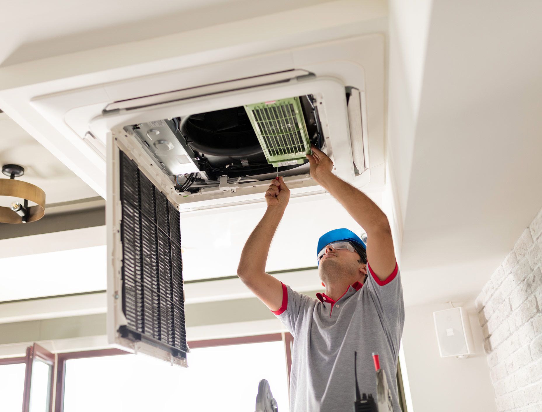 HVAC technician removing filter from ceiling air conditioning unit.