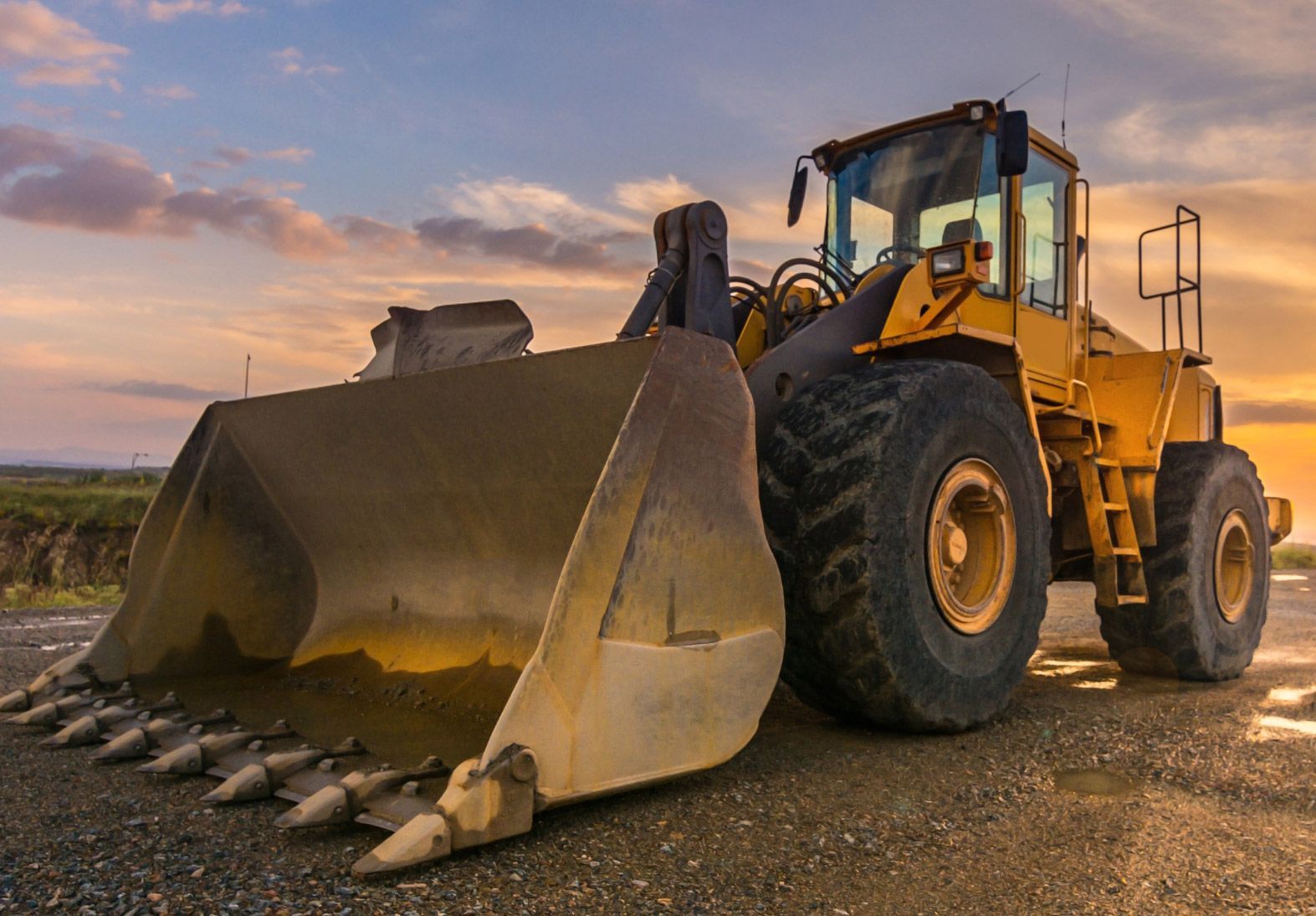 Yellow bulldozer with bucket raised, in a construction site at sunset.