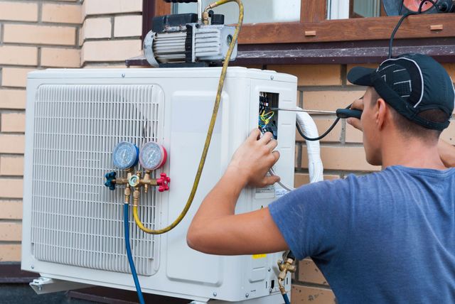 HVAC technician works on an outdoor air conditioning unit, using tools and gauges.