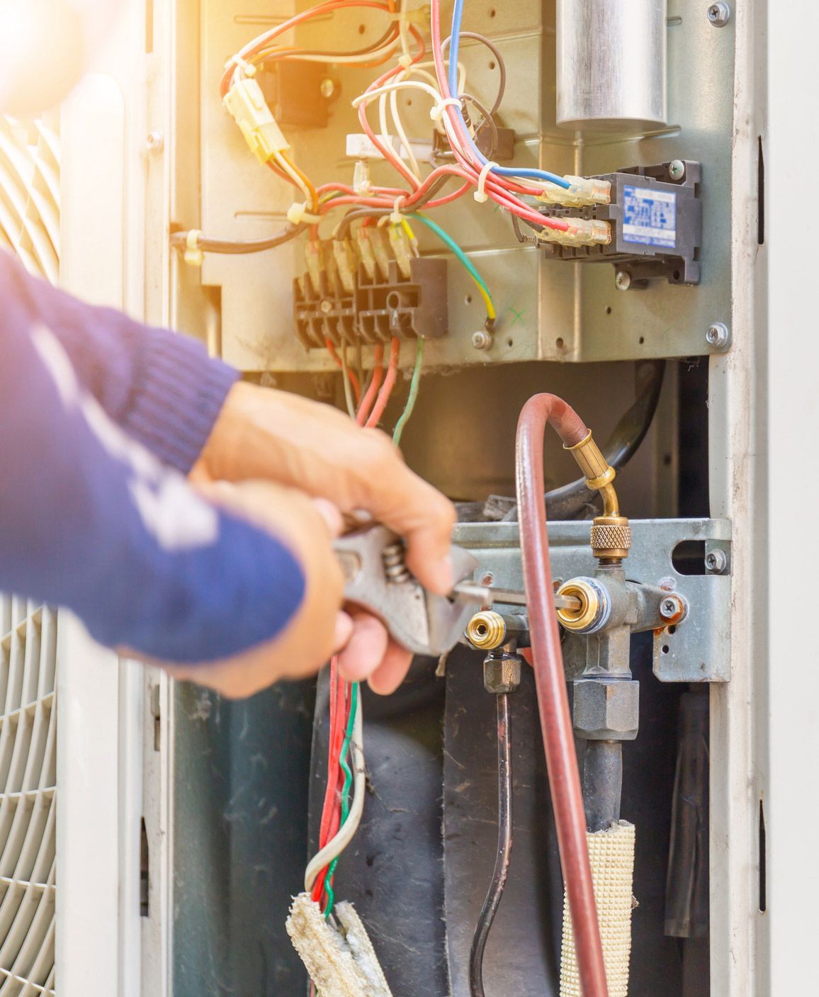 Person repairs an air conditioning unit with a wrench, focusing on valves and wiring.