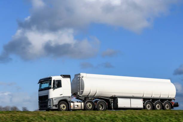 White tanker truck on a grassy roadside against a blue sky with clouds.