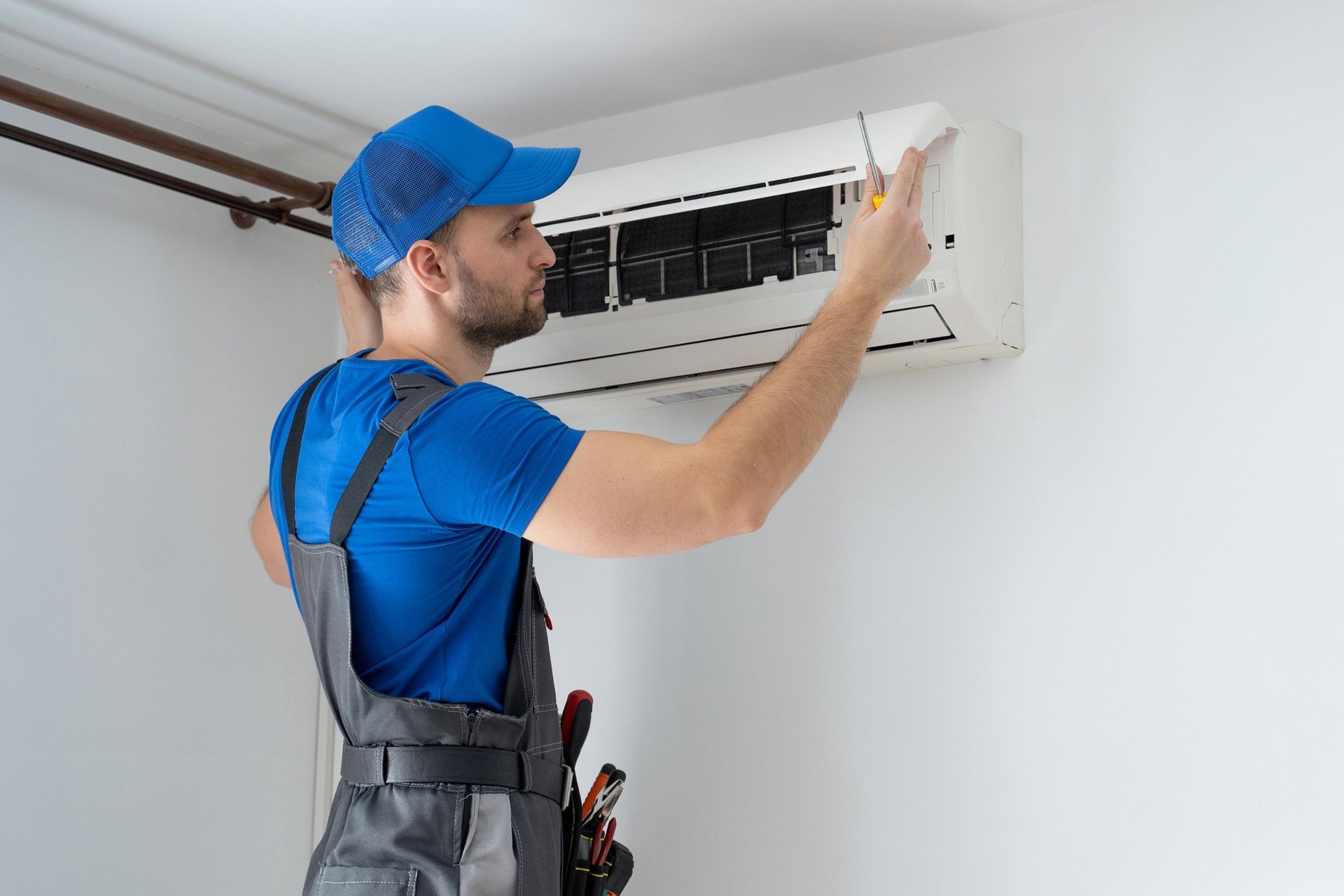 HVAC technician in blue uniform, fixing a wall-mounted air conditioner.