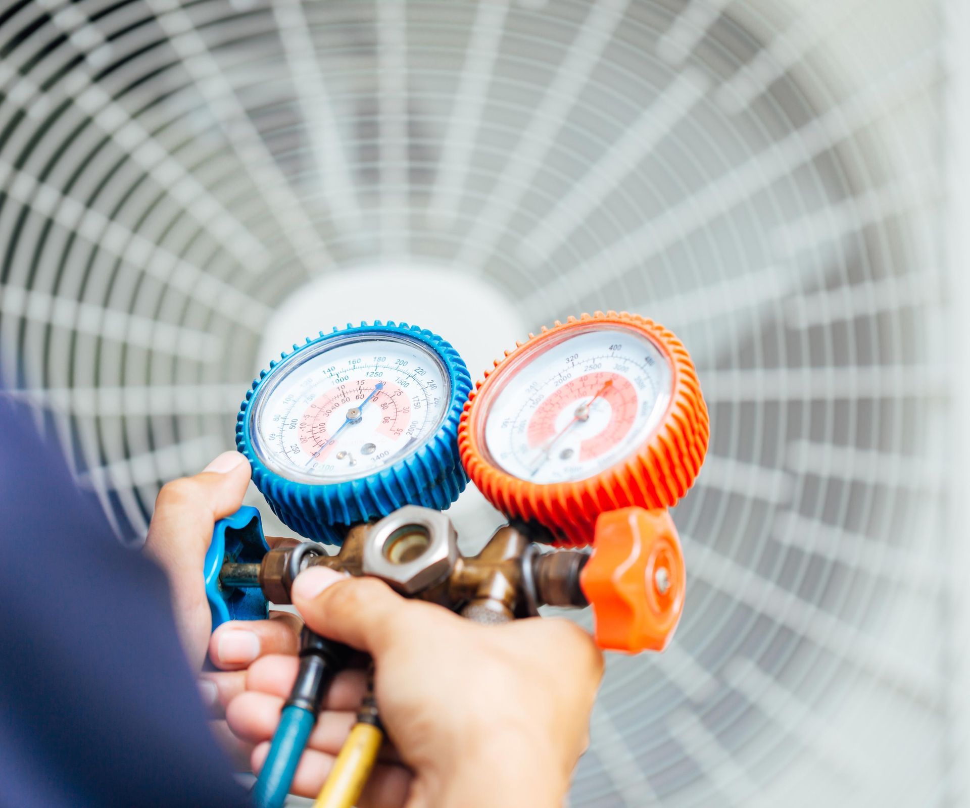 HVAC technician using gauges on an outdoor air conditioning unit to check pressure.