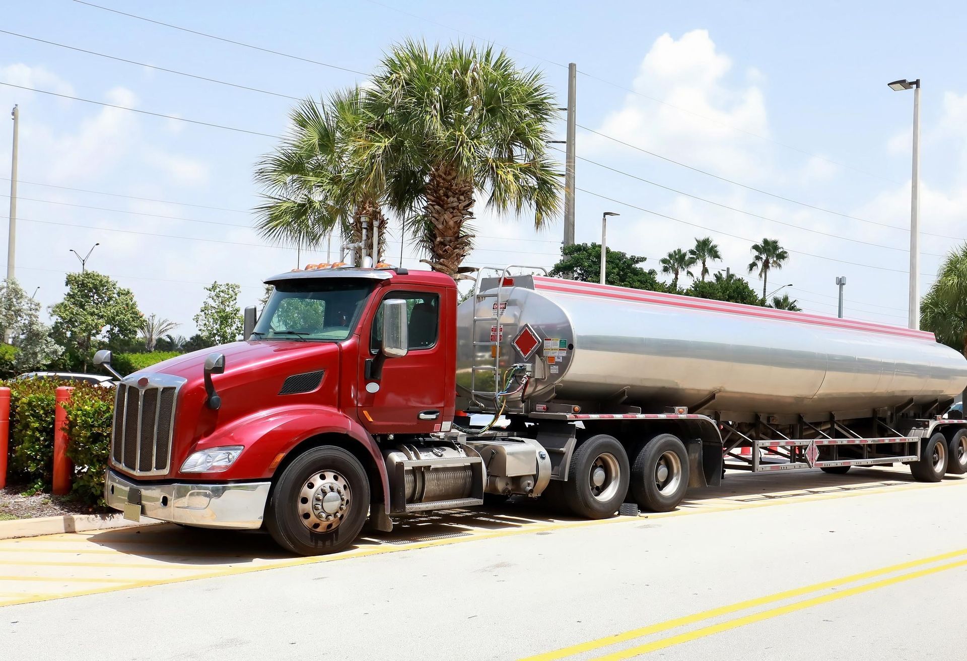 Red and silver tanker truck parked outdoors, near a building with palm trees.