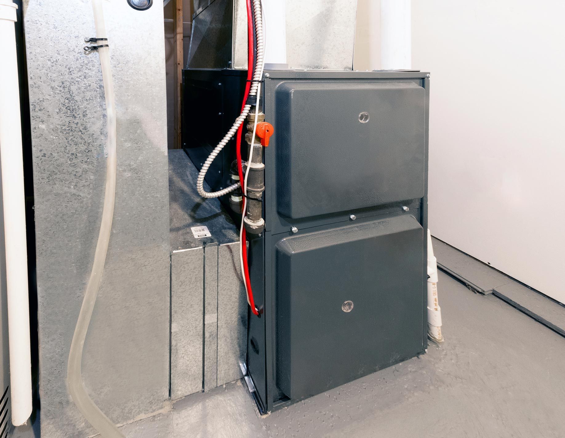 Gray furnace unit in a basement, with ductwork and pipes.