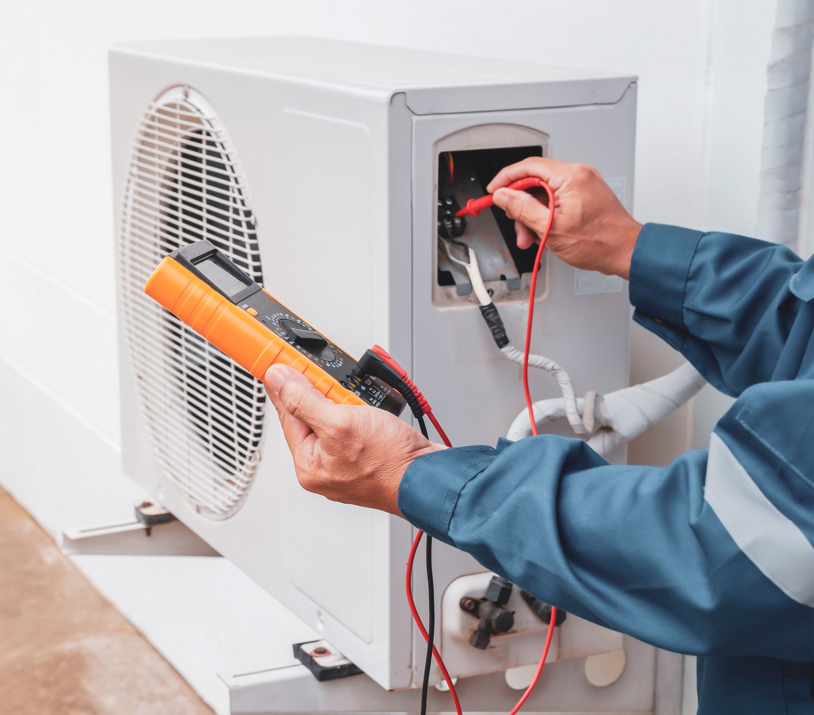 Mechanic uses a multimeter to test electrical wiring on an outdoor AC unit.