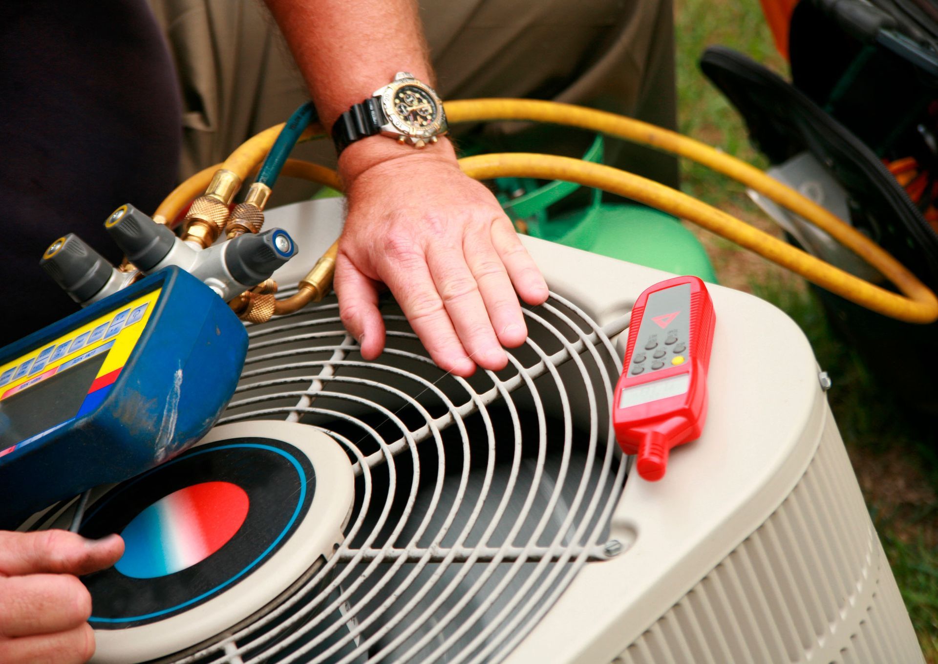 AC technician checking an outdoor unit with gauges and a thermometer.