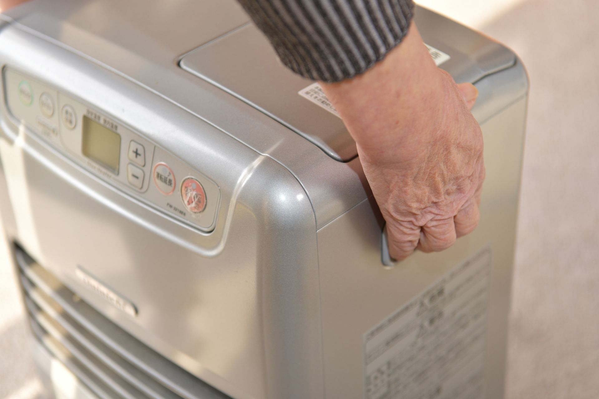 Person's hand on a silver space heater; pressing a side panel.