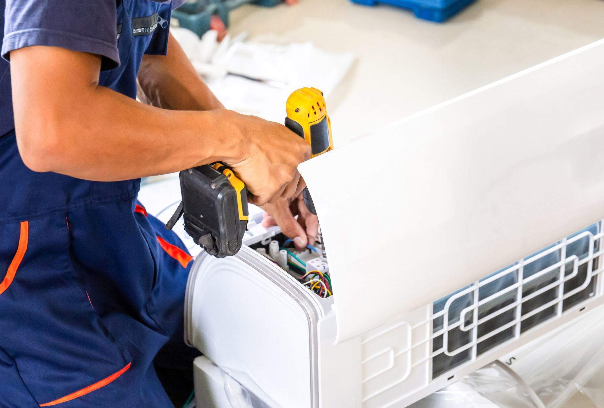 Person in blue overalls using a drill on an air conditioner unit.