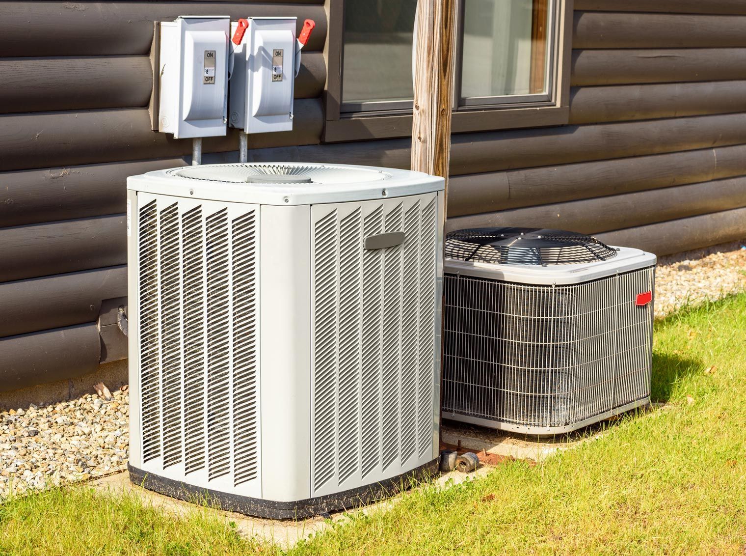 Two air conditioning units on a grassy lawn next to a dark brown building.