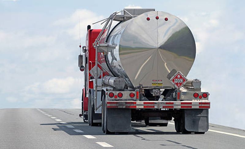 Red and silver tanker truck on a highway, transporting a flammable liquid, with a blue sky background.